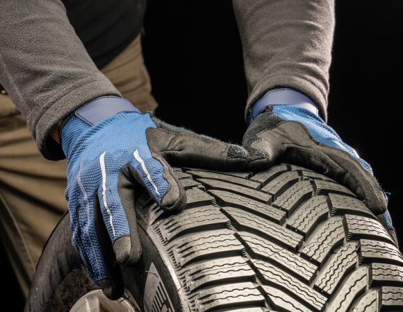 Close-up of man's hands pushing vehicle new tyre against black background.